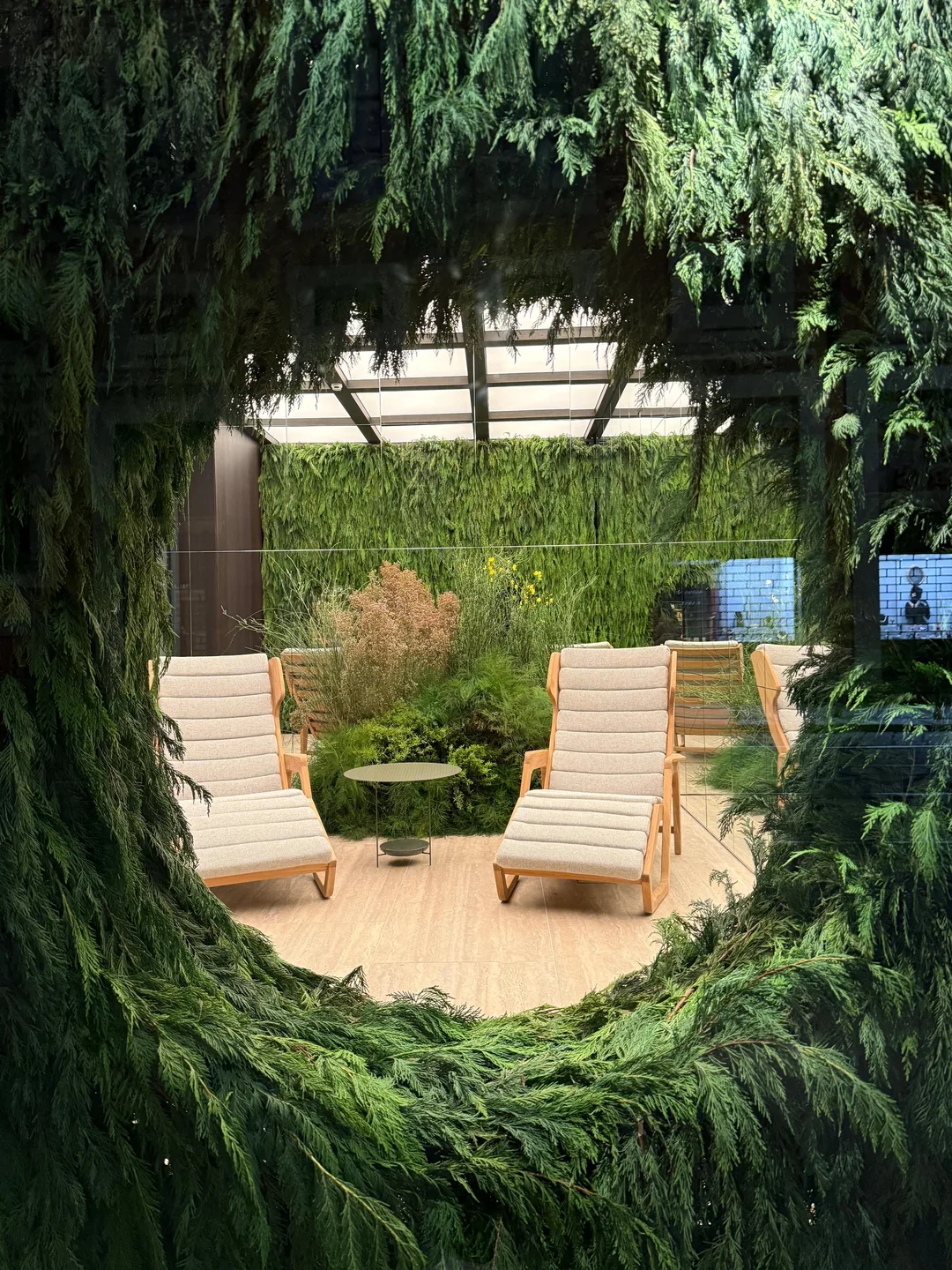 Jardim interno com mobiliário externo de madeira e vegetação na Semana de Design de Milão 2026